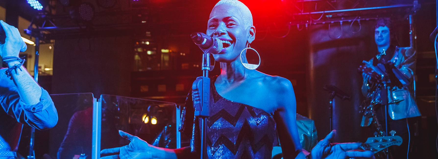 Female vocalist behind microphone singing with live band in background.